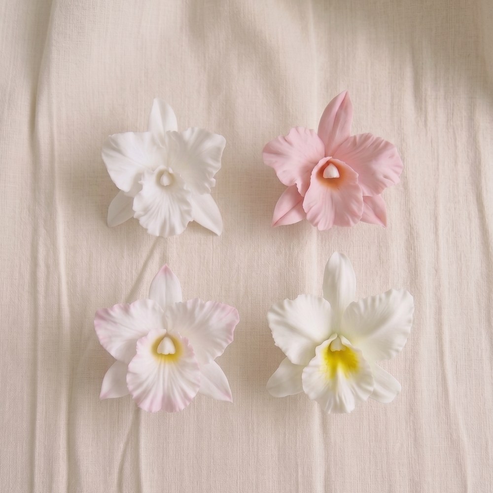 Four hand-sculpted cold porcelain cattleya orchids in Ivory White, Blush Pink, Ivory White with Blush Lip and Ivory White with Yellow Lip