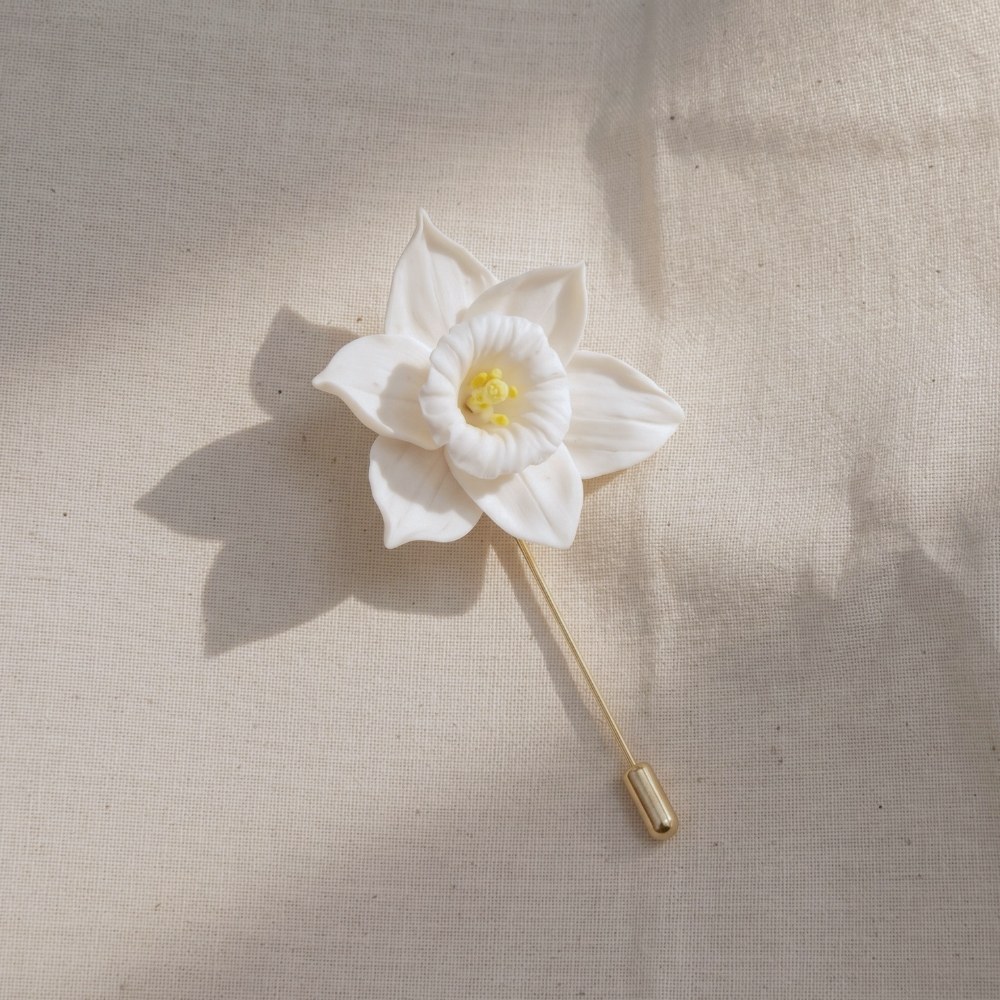 Ivory White cold porcelain daffodil lapel pin with a yellow stamen centre on a gold stick pin