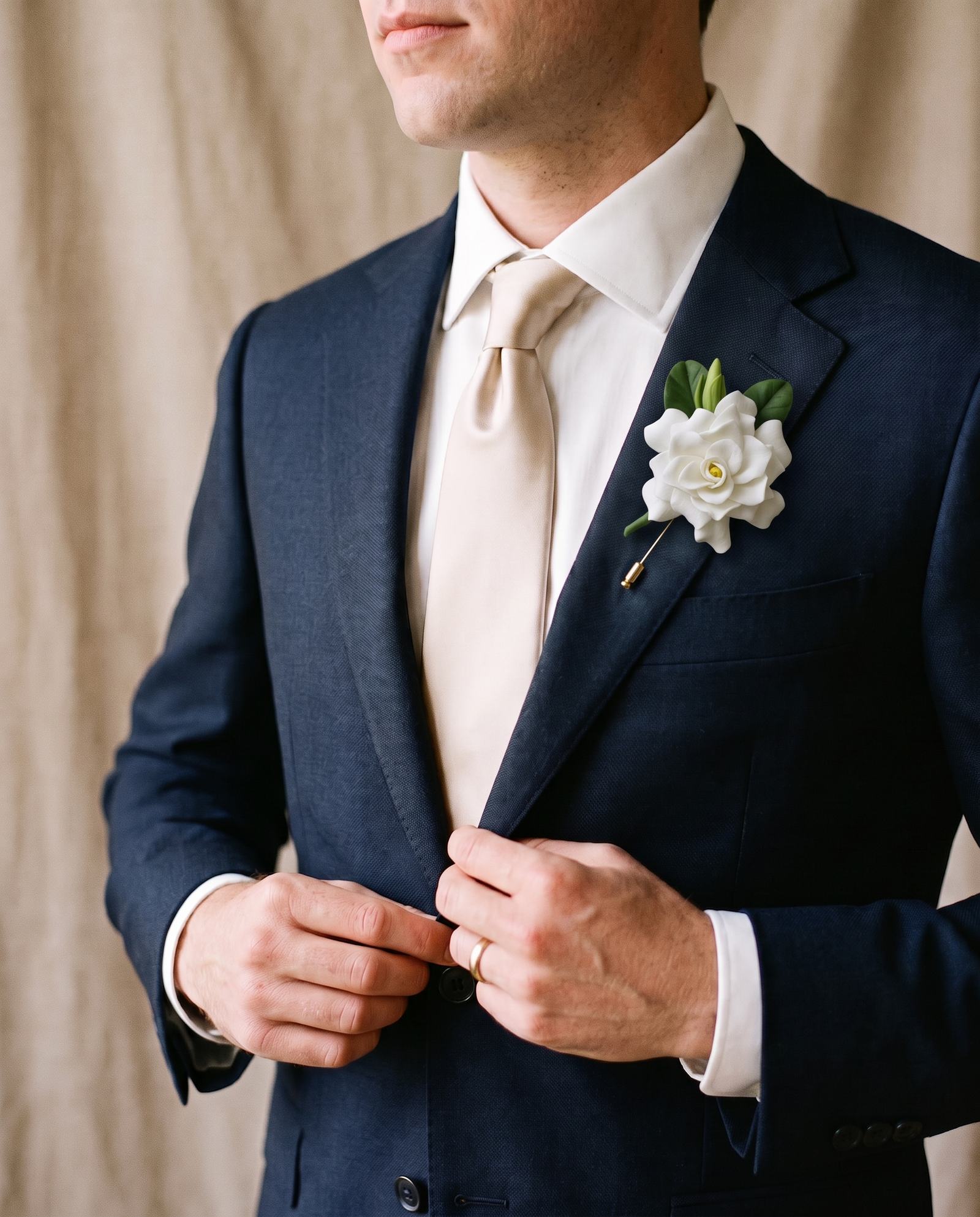 Ivory White cold porcelain gardenia lapel pin with green leaves on a groom's navy suit (real handmade flower, AI-generated setting)